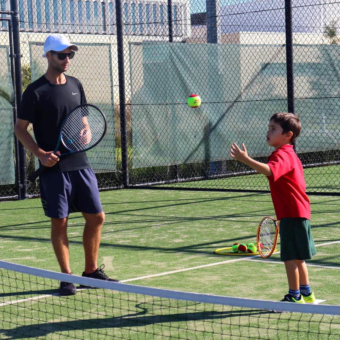 A young child playing tennis under a coach's supervision